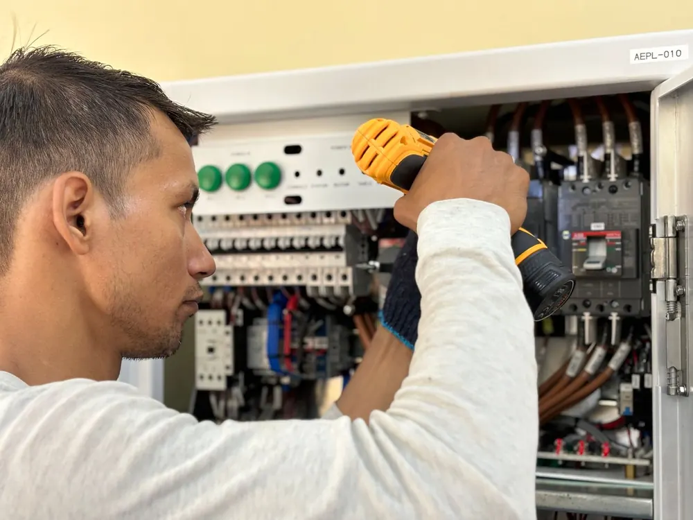 Electrician using a power drill inside an open breaker panel