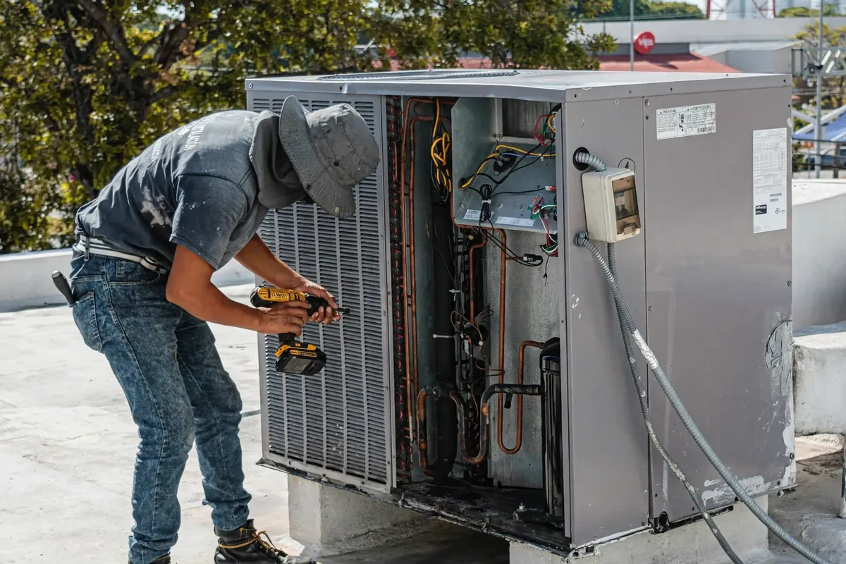 HVAC technician using a cordless drill to service a large outdoor air conditioning unit with its side panel open