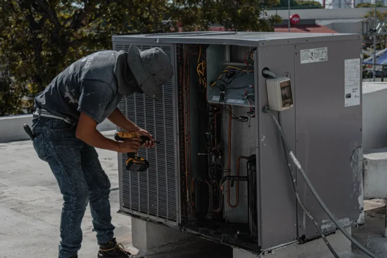 HVAC technician using a cordless drill to service a large outdoor air conditioning unit with its side panel open