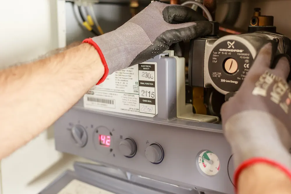 Gloved hands working on a boiler's controls during a service visit