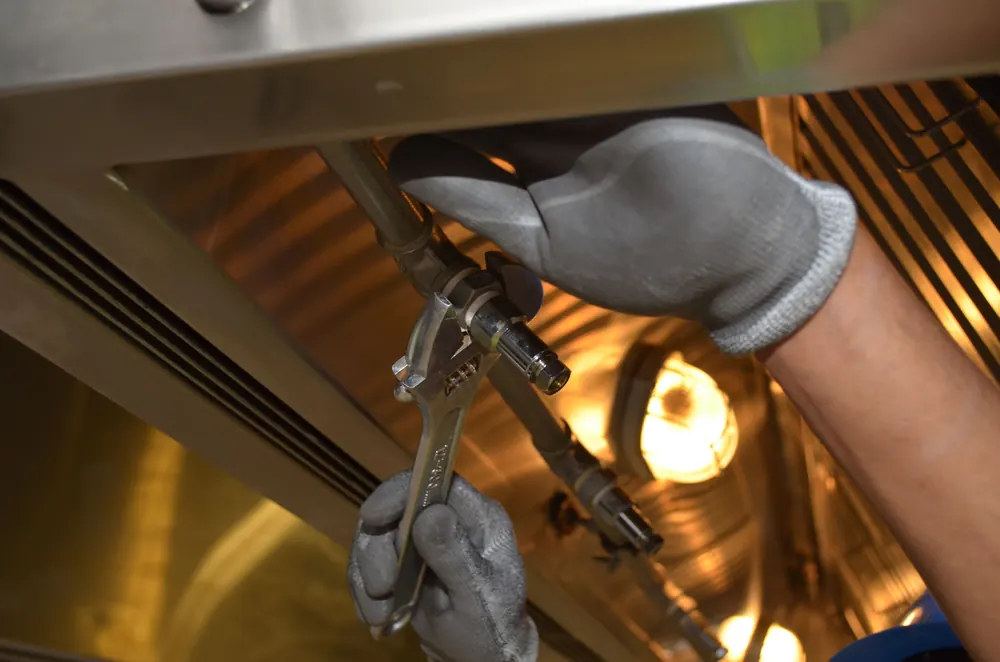 Plumber tightening a chrome pipe fitting with an adjustable wrench while clearing a blocked drain line
