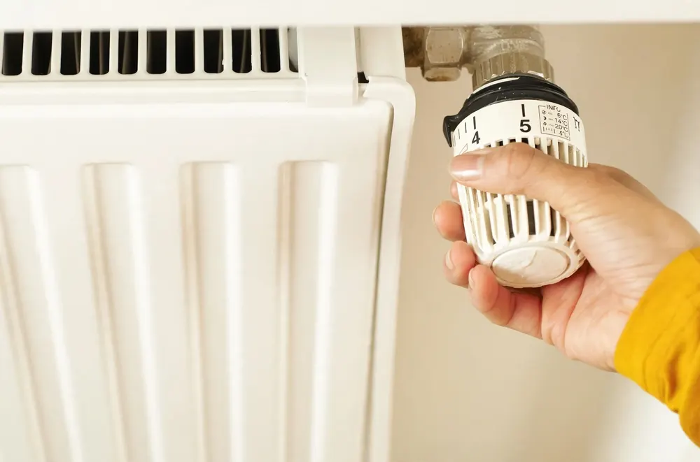 Hand adjusting a thermostatic radiator valve to control home heating