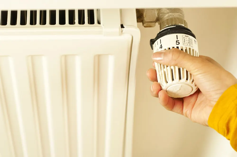 Hand adjusting a thermostatic radiator valve to control home heating