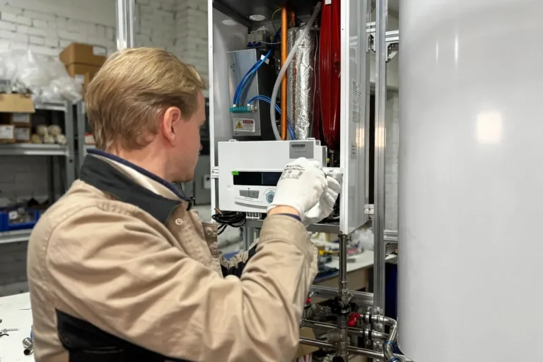Technician servicing an open wall-mounted heating unit next to a hot water storage tank