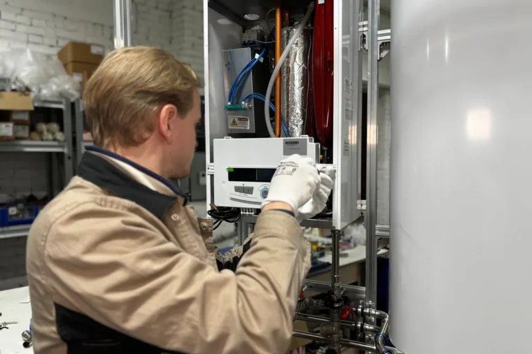 Technician servicing an open wall-mounted heating unit next to a hot water storage tank