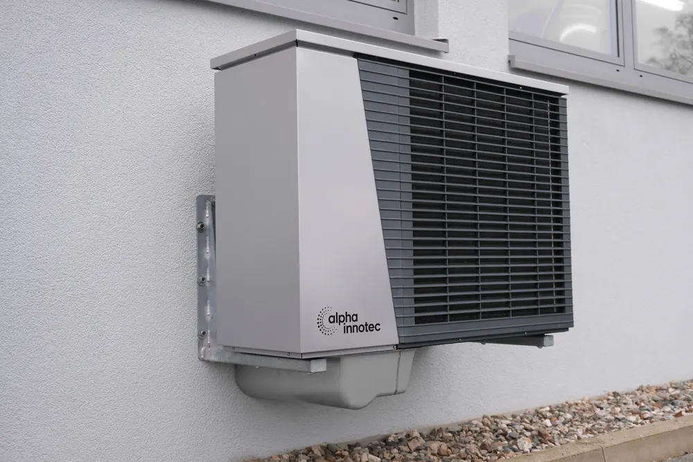Compact heat pump mounted on an outside wall, a common setup where yard space is tight