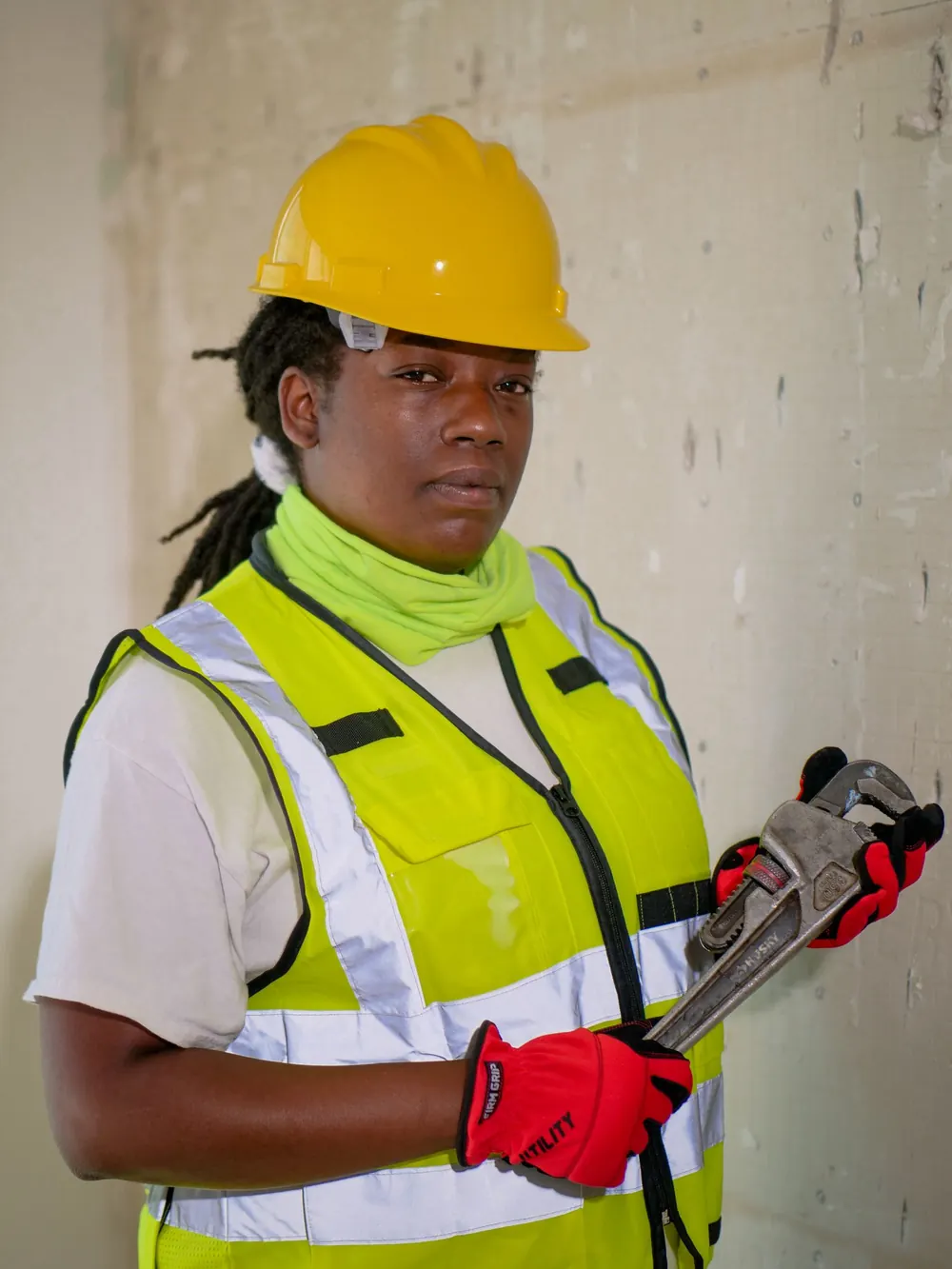 Plumber in a hard hat and safety vest holding a large pipe wrench