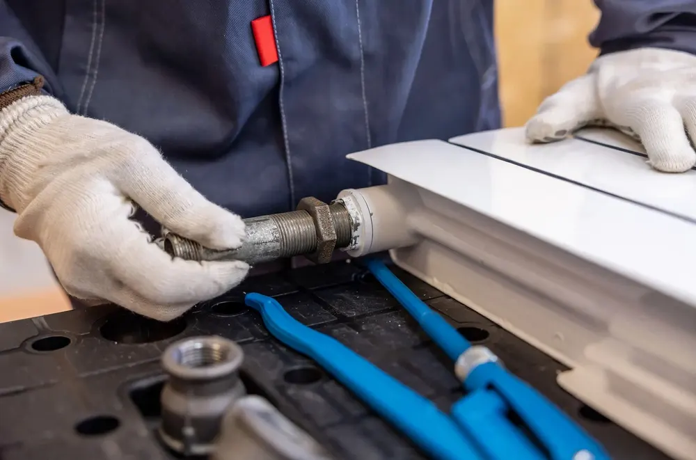 Plumber threading a steel pipe fitting by hand with pliers on the workbench