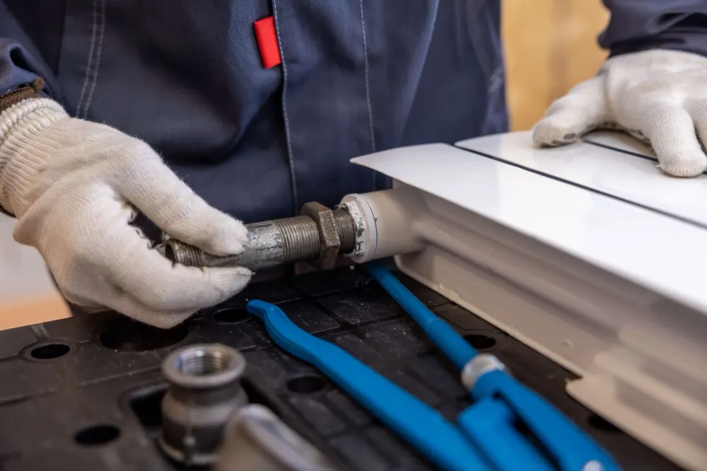 Plumber threading a steel pipe fitting by hand with pliers on the workbench