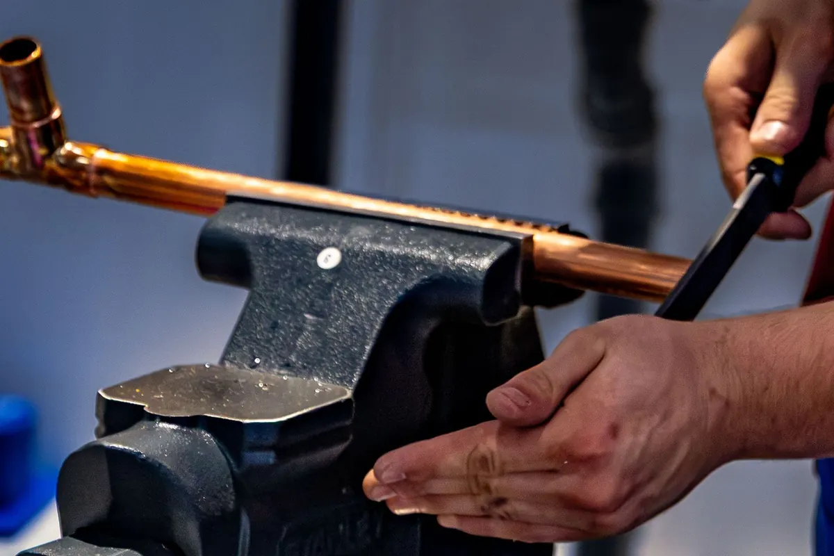 Plumber filing a copper pipe held in a bench vise