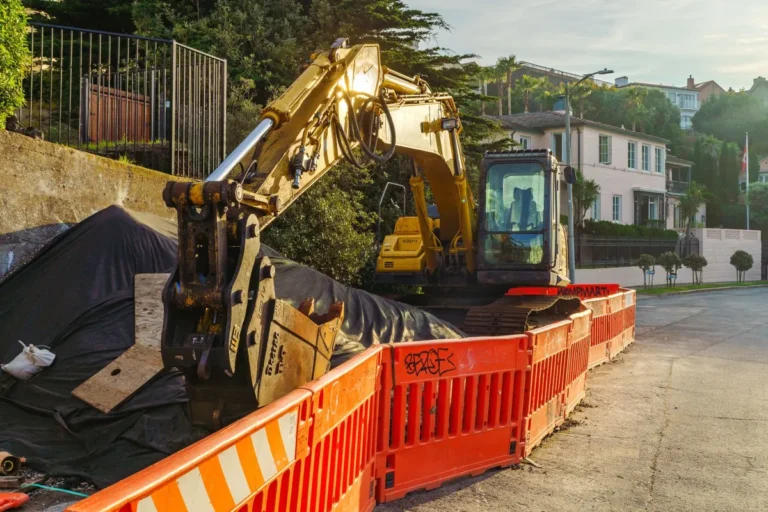 Excavator working behind orange safety barriers on a residential street during a sewer line replacement