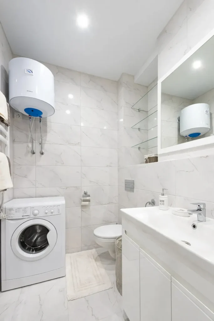 Wall-mounted tank water heater installed above a washing machine in a bathroom