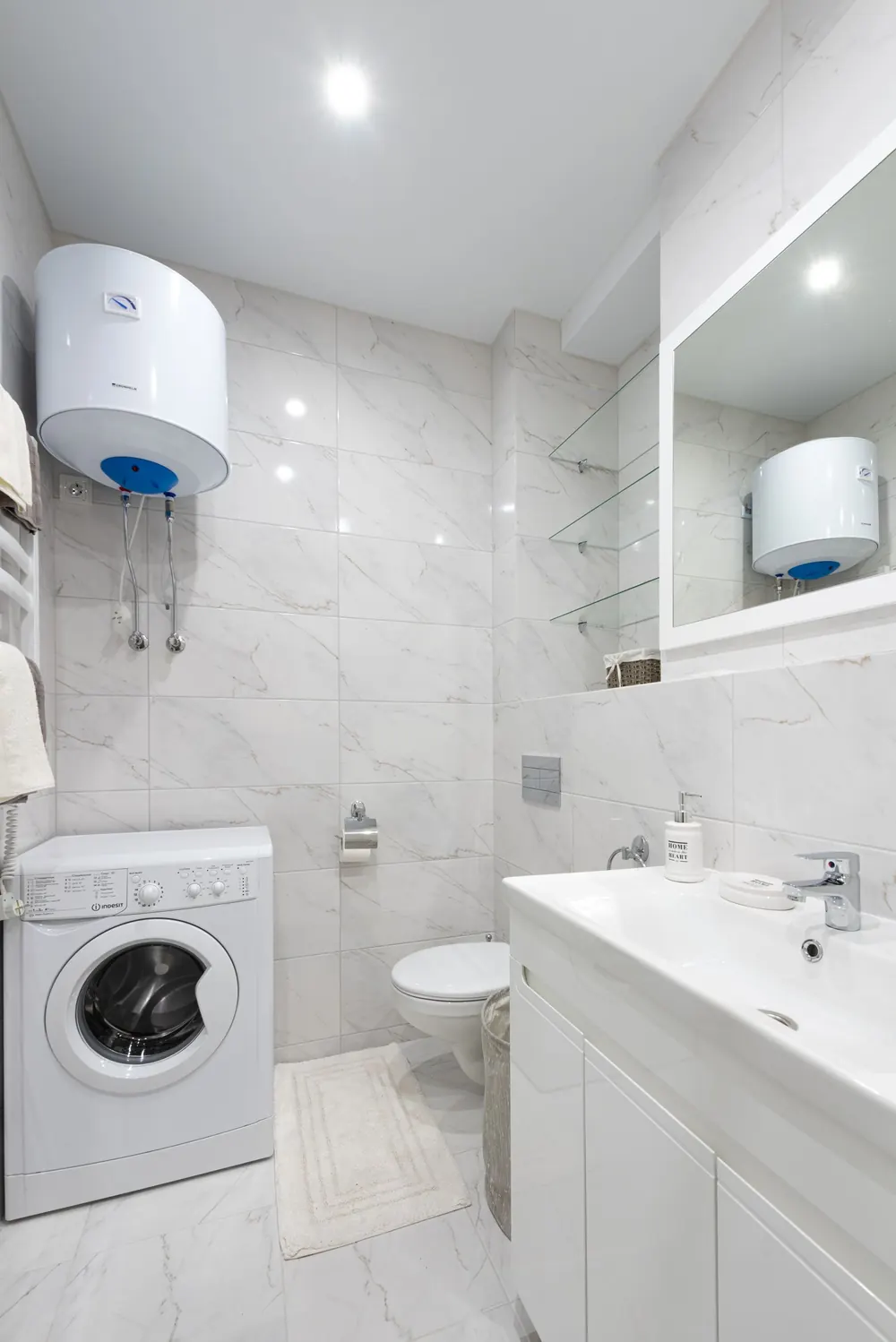Wall-mounted tank water heater installed above a washing machine in a bathroom